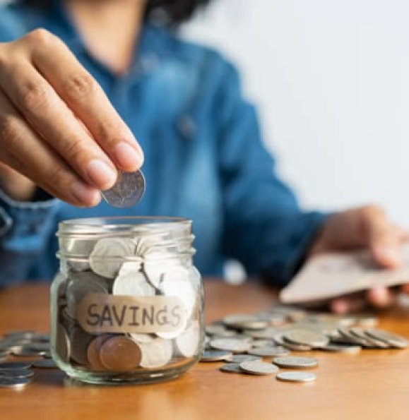 The woman hand is putting a coin in a glass  bottle and a pile of coins on a brown wooden table,Investment business, retirement, finance and saving money for future concept.