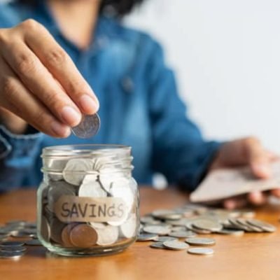 The woman hand is putting a coin in a glass  bottle and a pile of coins on a brown wooden table,Investment business, retirement, finance and saving money for future concept.
